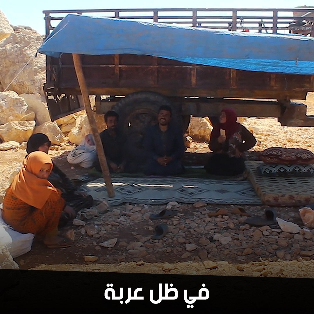 نازحون يقيمون في ظل عربة جرار زراعي يفترشون الأرض في مكان بائس